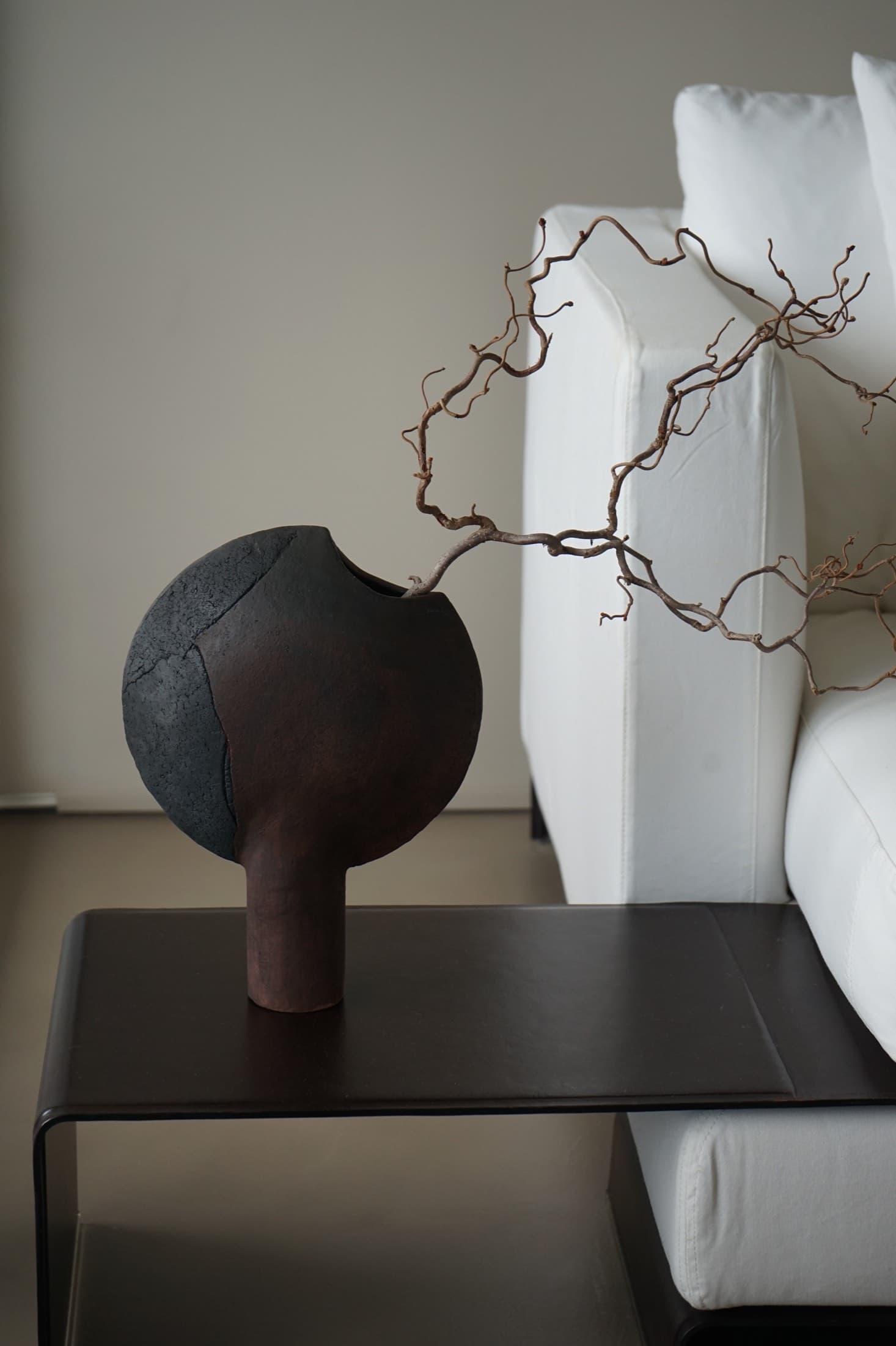 Moon-shaped vase in black and rust brown with a branch