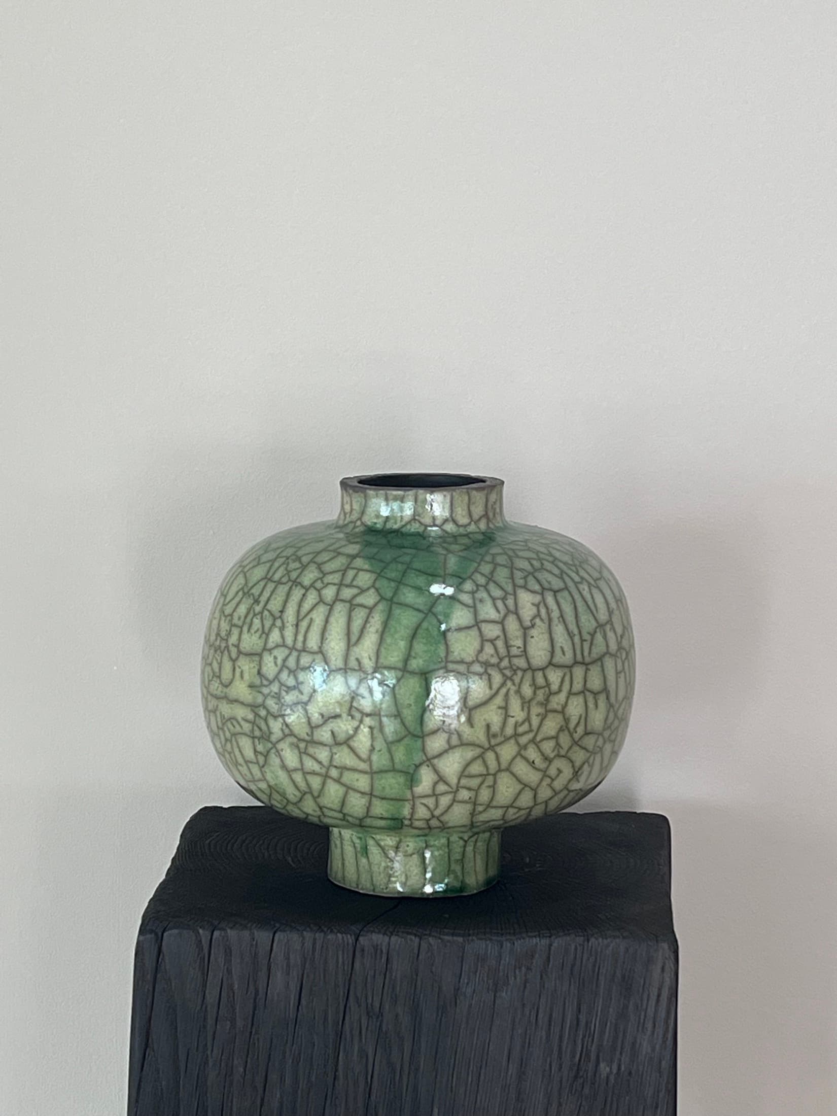 Round vase with a green crackle glaze on a dark pedestal