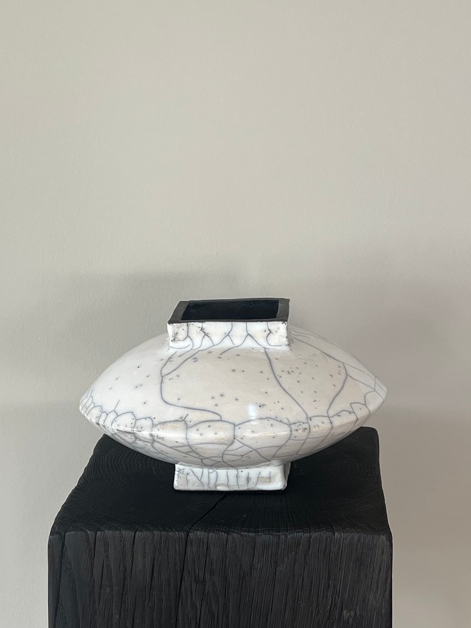 Disc-shaped vase with a white crackle glaze and a black opening