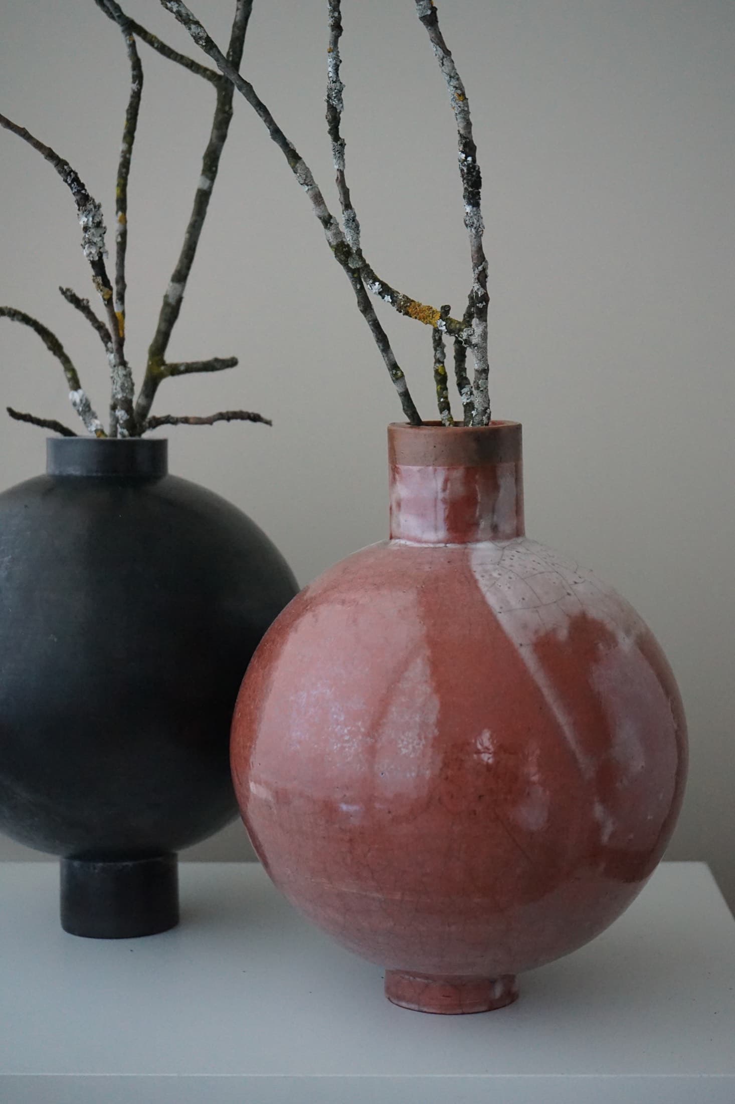 Two round vases in black and red with lichen-covered branches